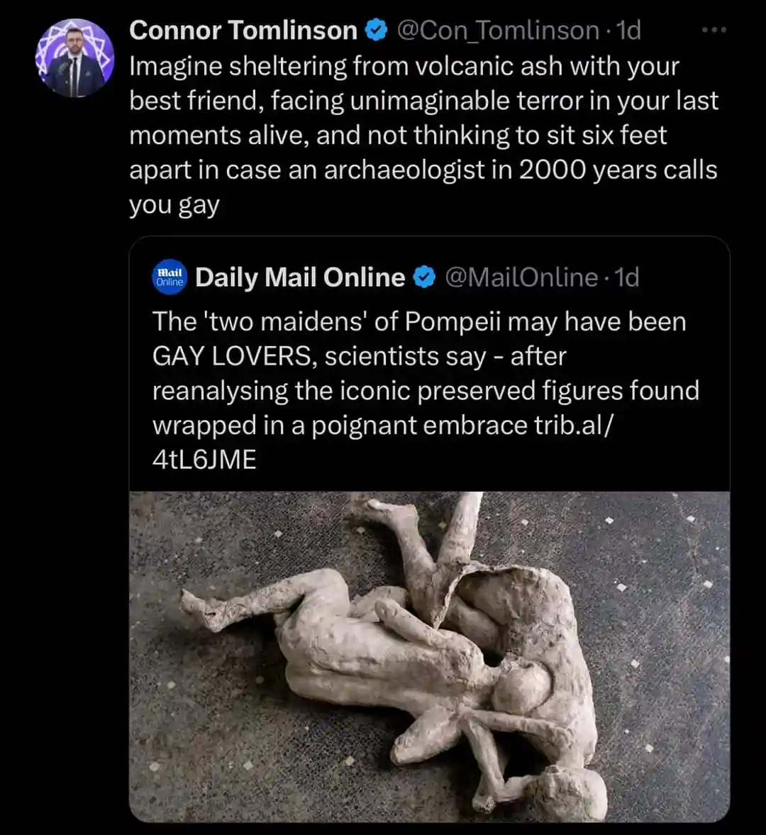 The image shows a grayscale photo of two preserved human figures from Pompeii, frozen in an intimate embrace, lying on a…