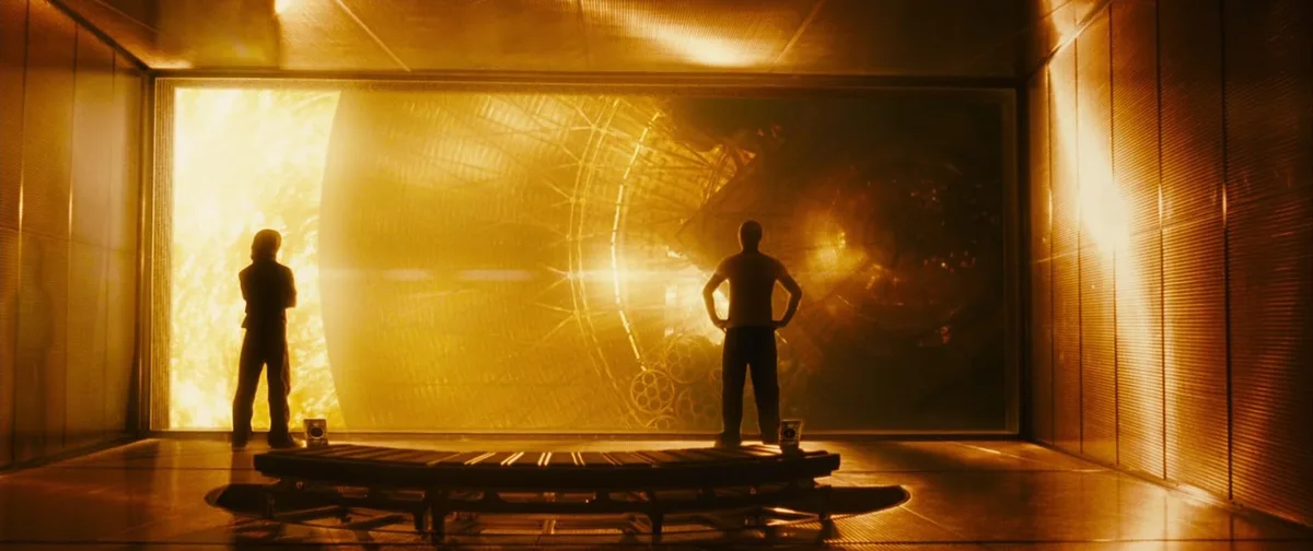 Two silhouetted men stand on a circular platform facing a massive, glowing golden portal or window in a futuristic room. One…