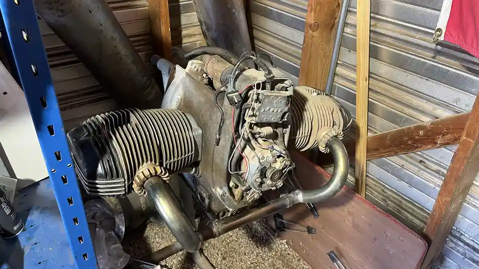 A dusty, disassembled vintage aircraft engine sits on a workbench in a cluttered garage, surrounded by tools and metal…