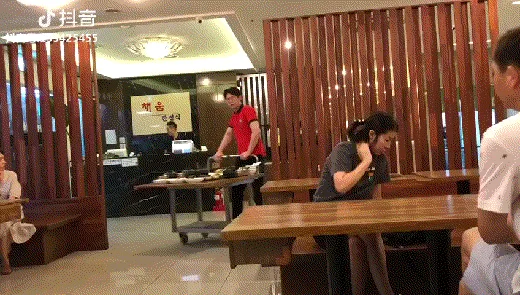 A sequence of images shows a waiter in a red shirt serving an extremely large, elaborate Korean meal to a seated customer in…