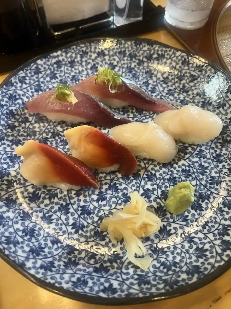 A plate of nigiri sushi with various fish toppings, including tuna and scallop, arranged on a blue and white patterned…