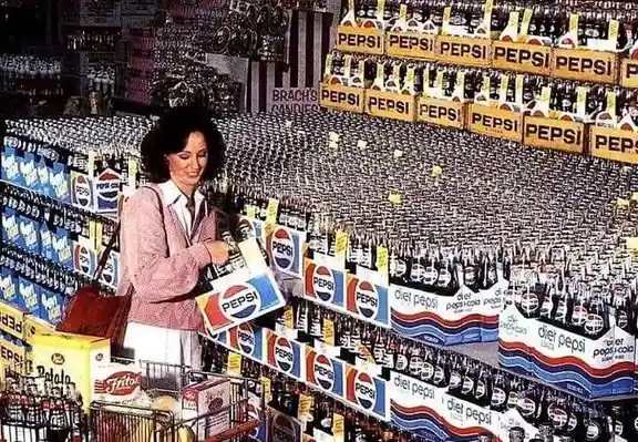 A woman in a pink jacket stands in a supermarket aisle surrounded by towering shelves of Pepsi products, including bottles…