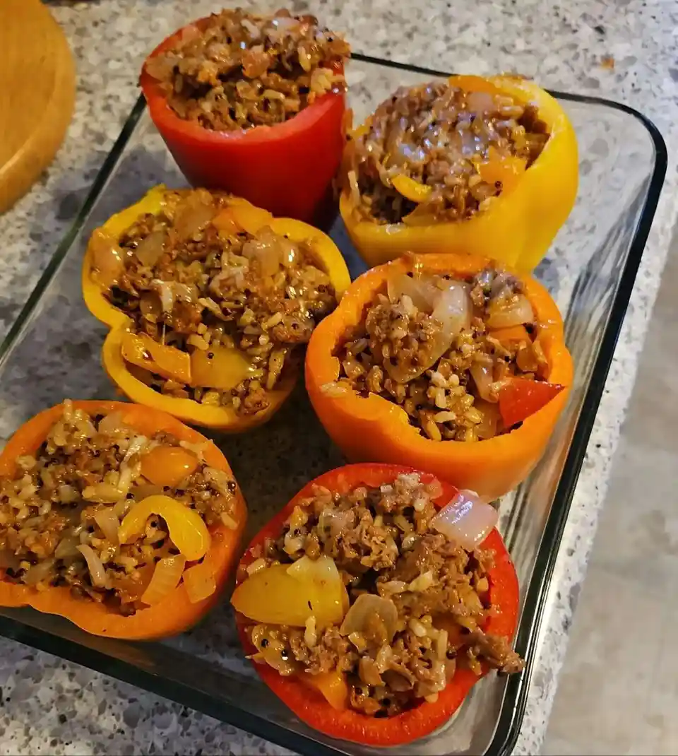 A glass baking dish holds six colorful bell peppers—red, orange, and yellow—each hollowed out and filled with a savory…
