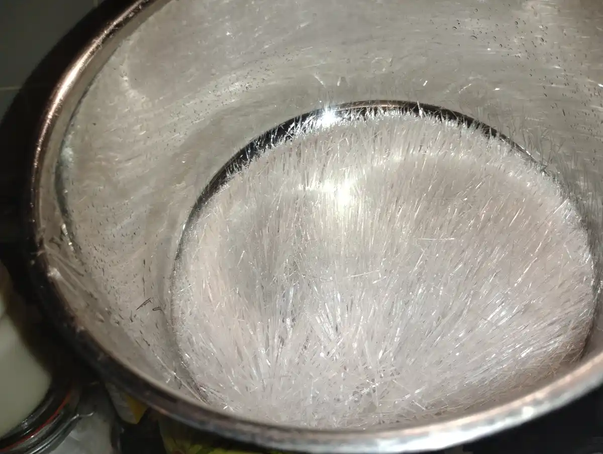 A close-up photo shows the inside of a stainless steel pot covered in a dense layer of sharp, needle-like ice crystals, with…