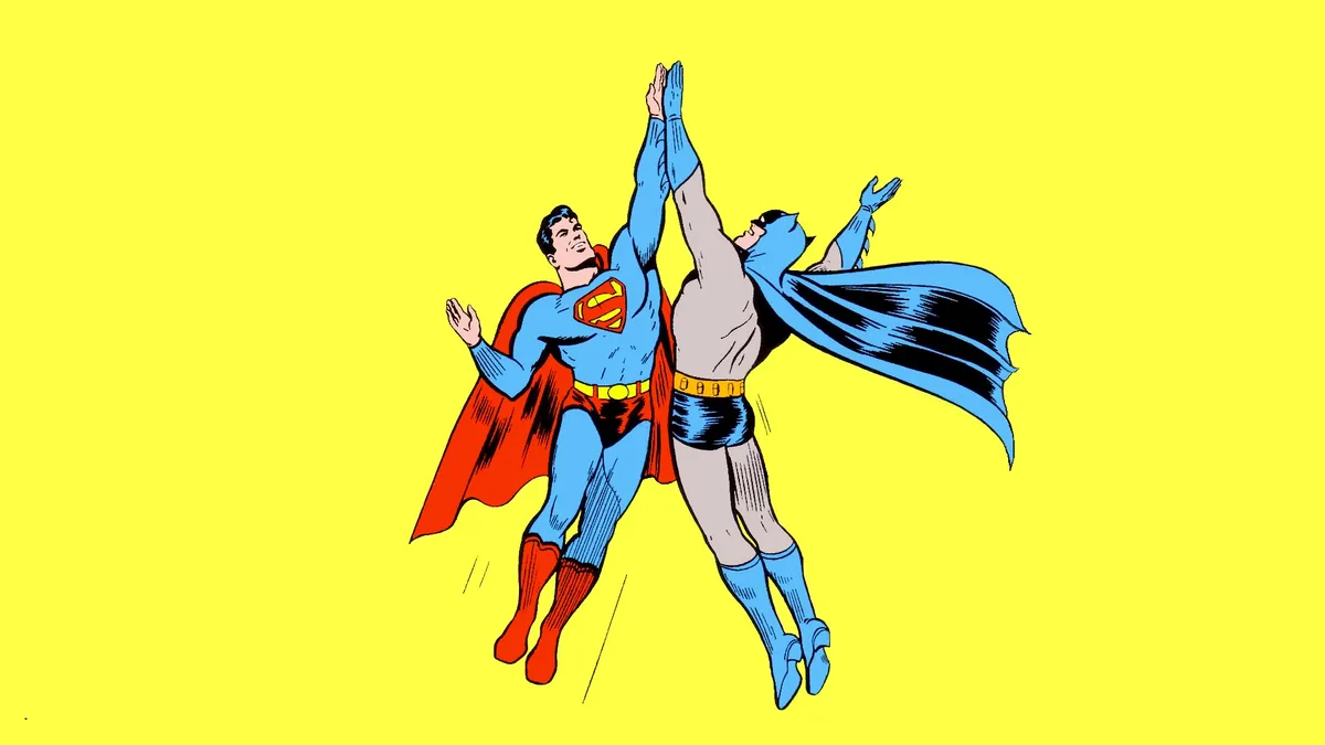 Two comic book superheroes, Superman in his blue suit with red cape and Batman in his grey suit with blue cape, are shown…