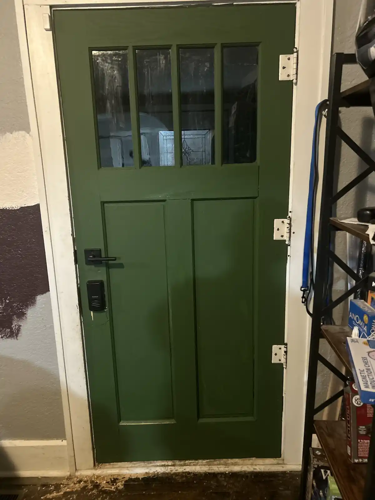 A close-up photo of a green front door with four glass panes in the upper half and a black electronic lock. The door is set…