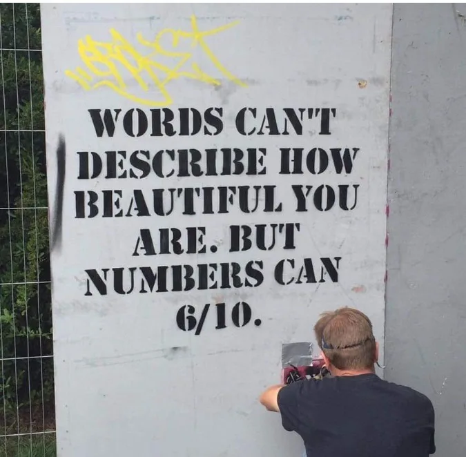 A person is seen from behind, applying a stencil to a concrete wall. The stencil reads 'WORDS CAN'T DESCRIBE HOW BEAUTIFUL…