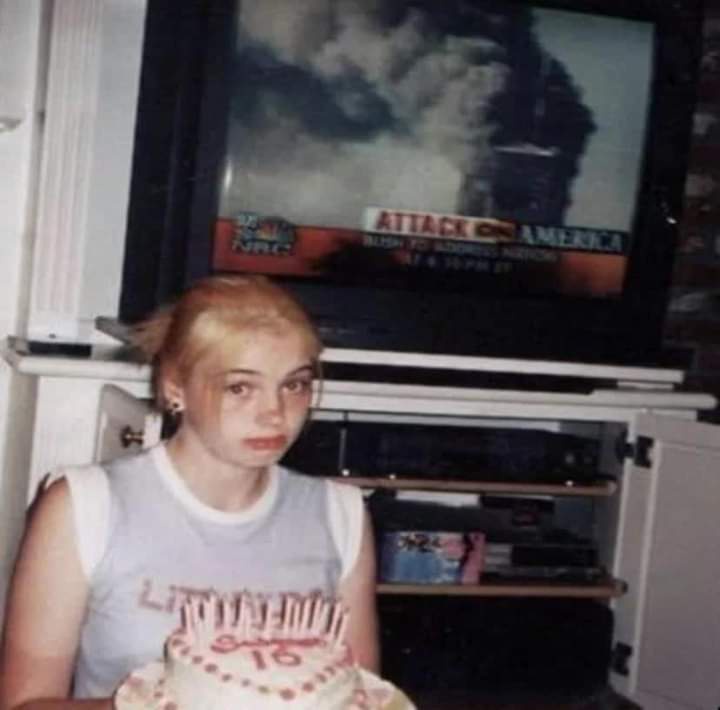 A young girl with blonde hair, wearing a white tank top, holds a birthday cake with candles and the number 16 written on it…