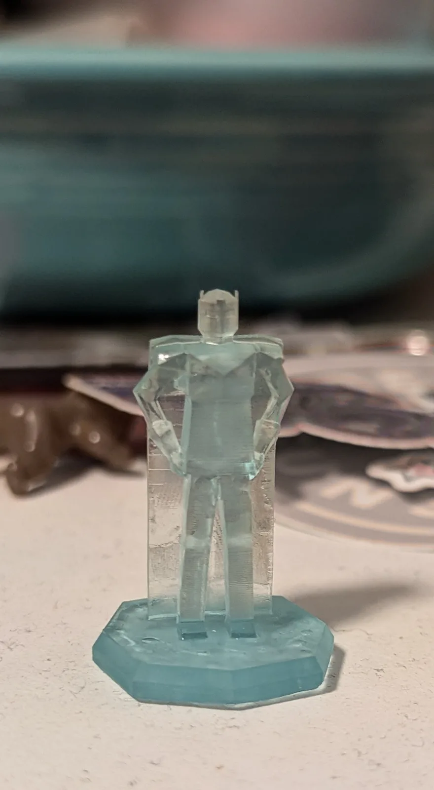 A translucent, light-blue 3D-printed figurine of a humanoid with a blocky, angular design stands on a matching octagonal…