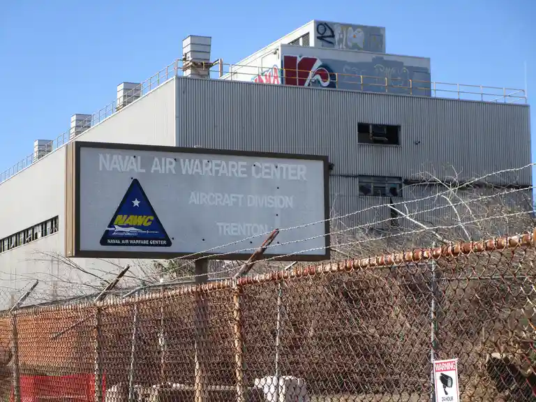 A large sign for the Naval Air Warfare Center Aircraft Division in Trenton is mounted in front of a large industrial…