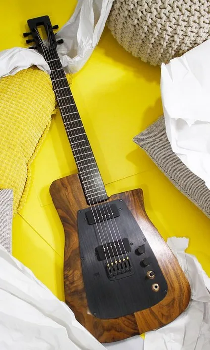A black and wood-finish electric guitar with a face-like design on its body lies on a bright yellow surface surrounded by…