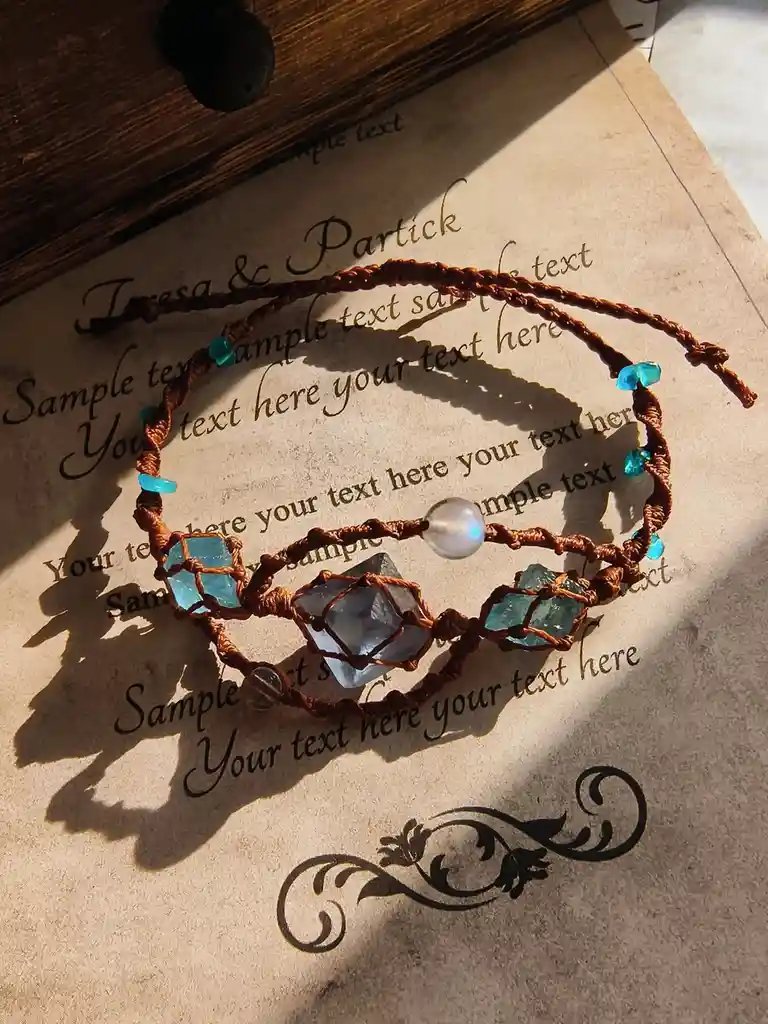 A brown macrame-style bracelet with blue and clear gemstones rests on a piece of paper with placeholder text like 'Sample…