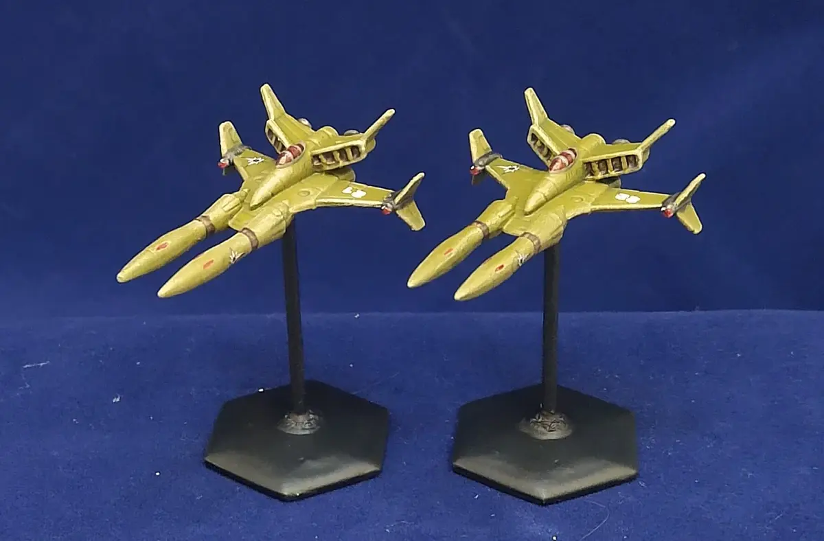 Two identical yellow model fighter jets, each mounted on a black hexagonal stand, are positioned side-by-side against a…