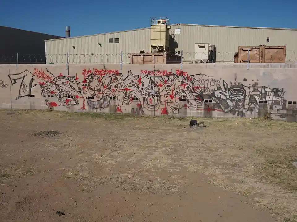 A concrete wall covered in large, stylized graffiti art with black and red spray paint, featuring aggressive lettering and a…