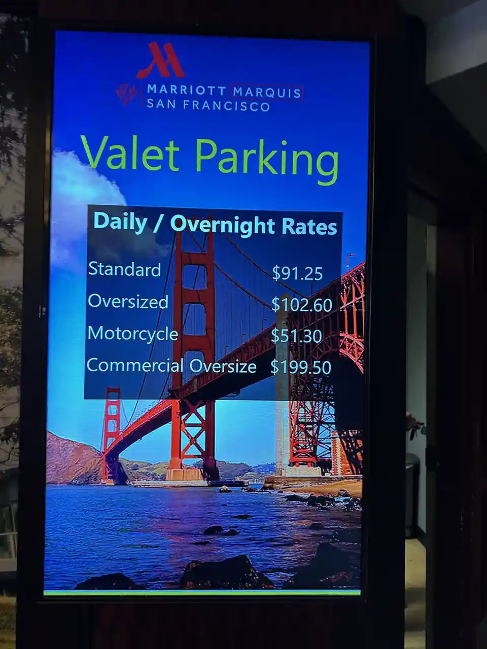 A digital sign for the Marriott Marquis San Francisco displays valet parking rates against a backdrop of the Golden Gate…
