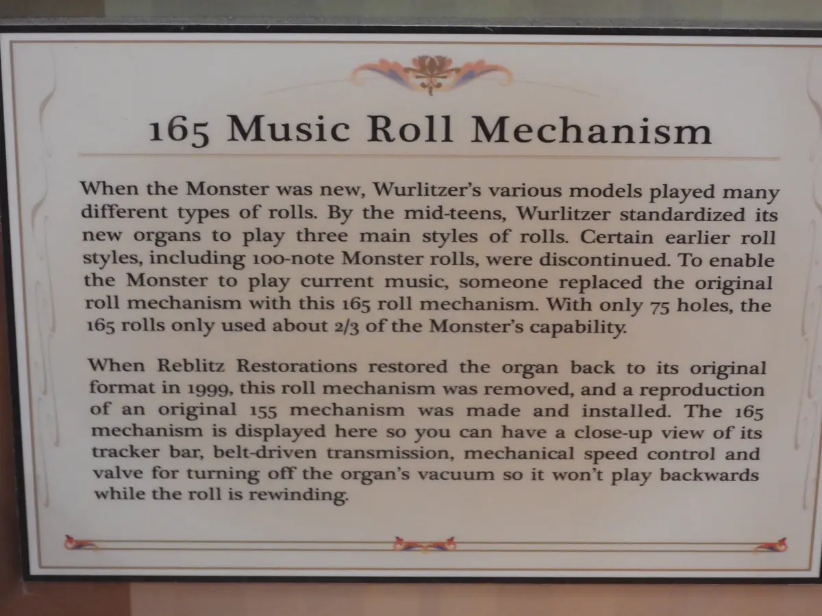 A museum plaque titled '165 Music Roll Mechanism' explains that this mechanism, with only 75 holes, was installed to play…