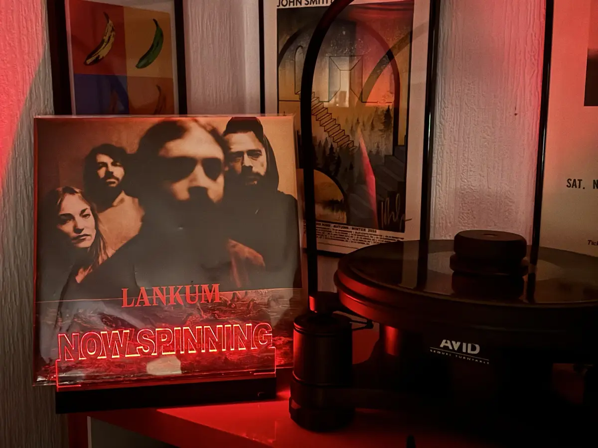 A red-lit vinyl record player sits next to a glowing neon sign displaying 'LANKUM NOW SPINNING' over a photo of the band…