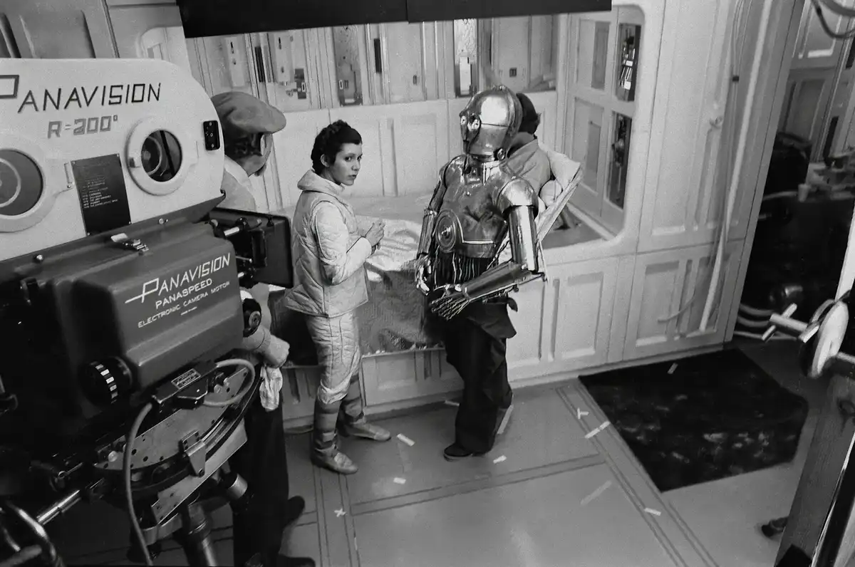 A black-and-white behind-the-scenes photo from the Star Wars film set shows actress Carrie Fisher as Princess Leia and actor…