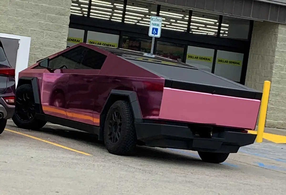 A pink and black Tesla Cybertruck is parked in a designated reserved handicapped parking spot in front of a Dollar General…