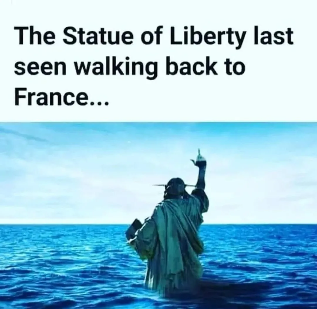 The image shows the Statue of Liberty standing waist-deep in the ocean, facing away from the viewer, with its torch raised…