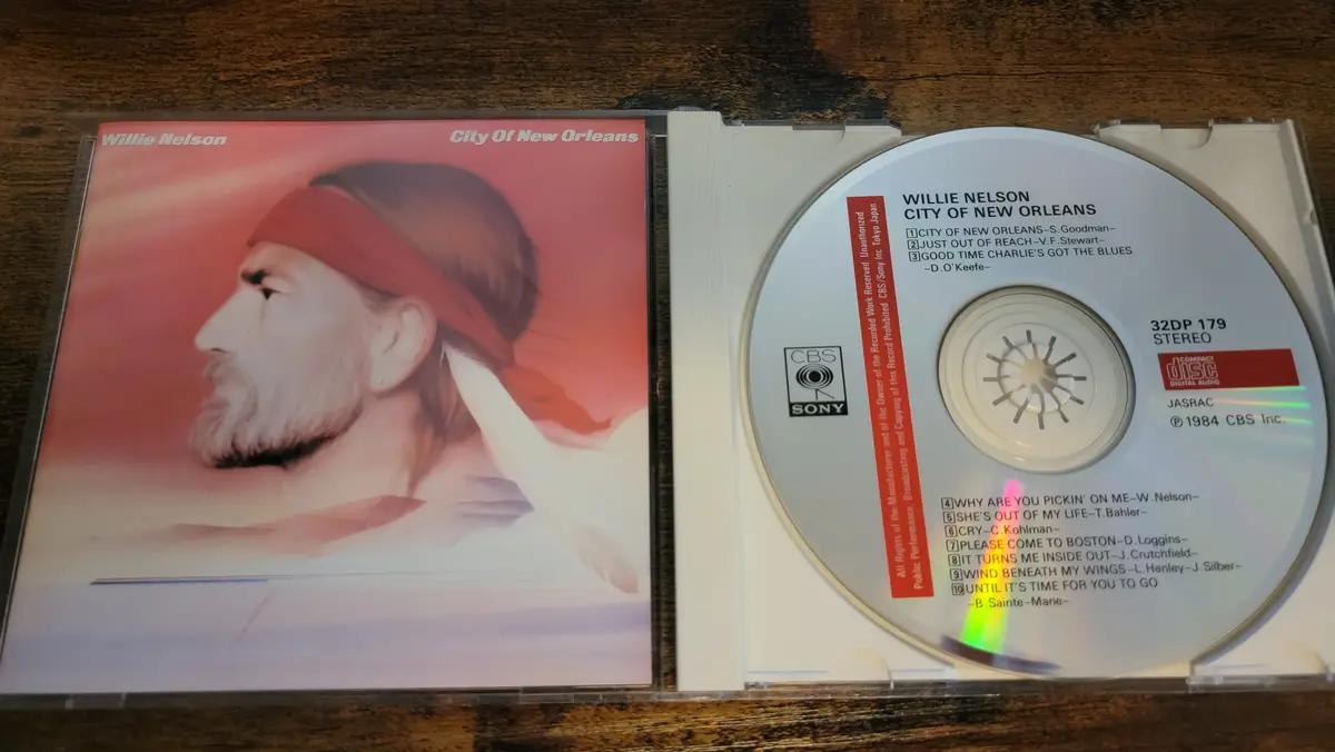 A physical CD case for Willie Nelson's 1984 album 'City of New Orleans' is open, showing the album cover with a painted…