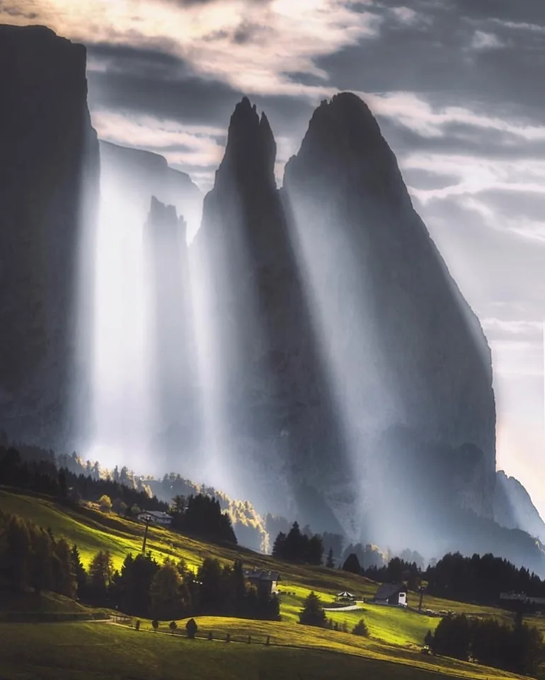 A dramatic landscape photo shows towering, jagged rock formations under a cloudy sky with beams of sunlight piercing…