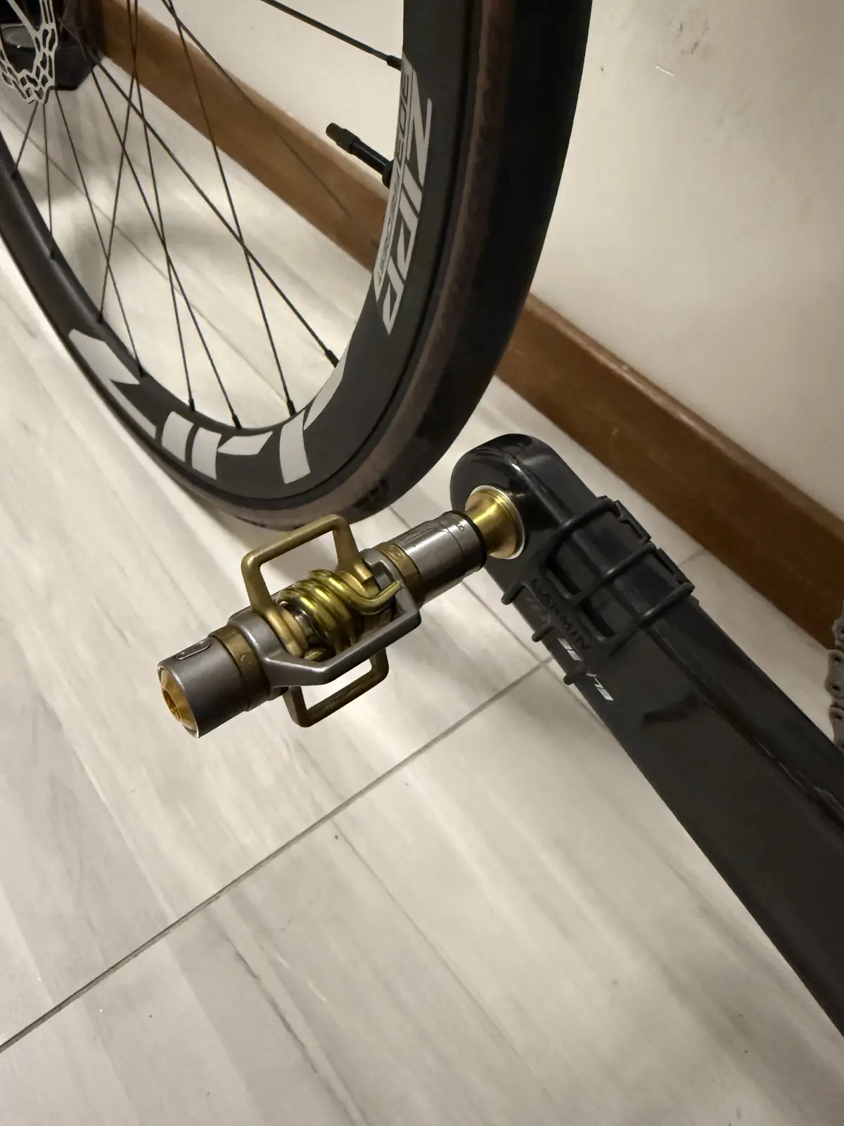 A close-up photo shows a bicycle's rear wheel and a custom brass pedal attached to the crank arm, with the pedal's metallic…