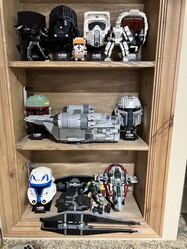 A wooden shelf display holds multiple Star Wars-themed LEGO collectibles, including character heads like Darth Vader, Boba…