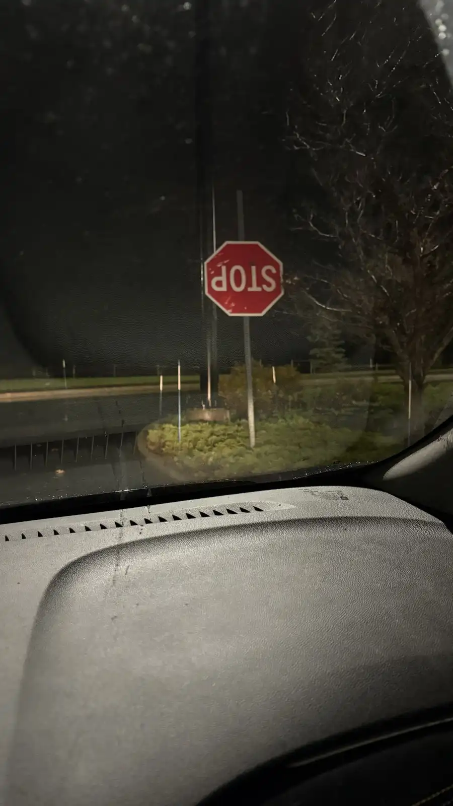 A nighttime photo taken from inside a car shows a red octagonal stop sign viewed through a rain-speckled windshield. The…