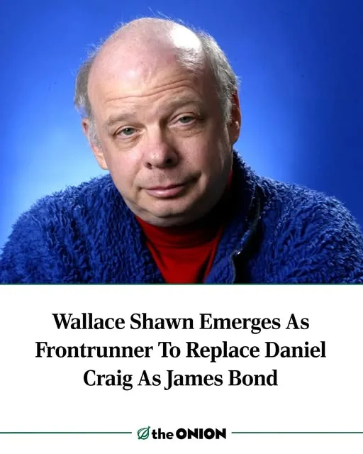 A headshot of actor Wallace Shawn, who has a balding head and is wearing a blue fuzzy jacket over a red turtleneck, set…
