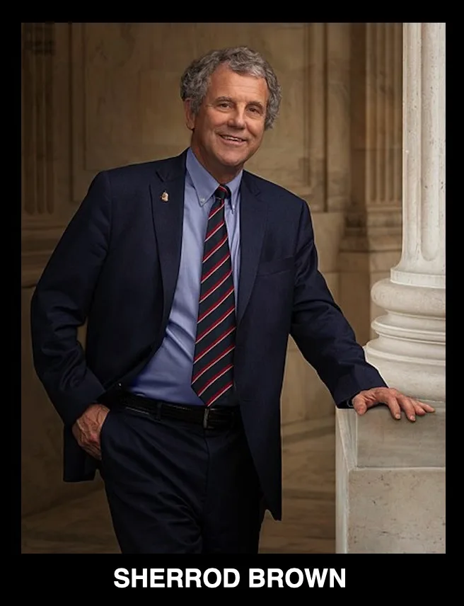 A formal portrait of a smiling man with gray hair wearing a dark suit, light blue shirt, and a red-and-blue striped tie…
