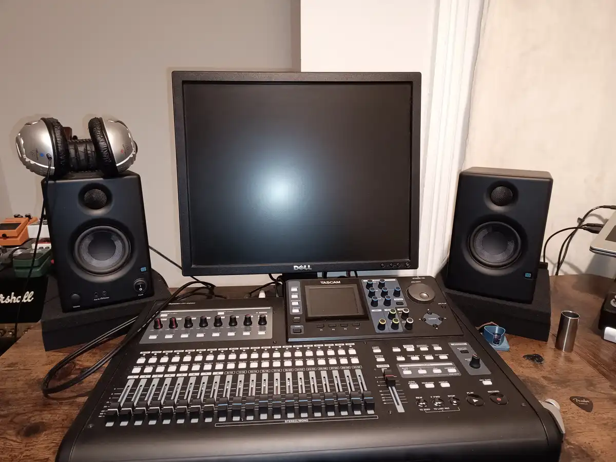A photo of a home studio setup featuring a Tascam audio interface, a Dell monitor, and two studio monitors with headphones…