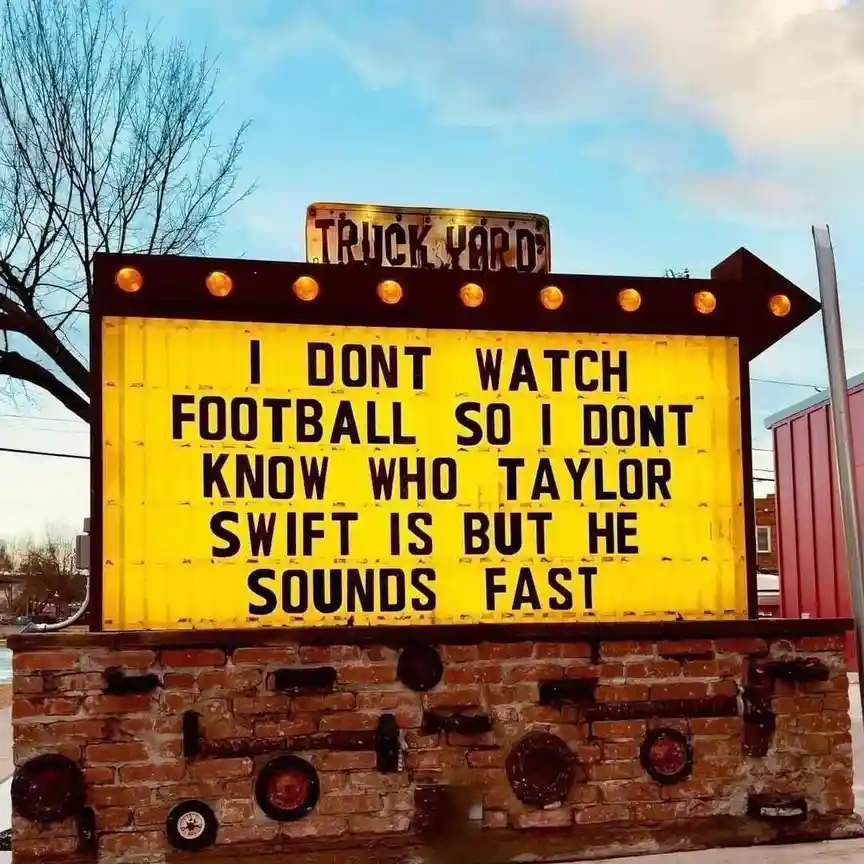 A yellow marquee sign with black text reads 'I DONT WATCH FOOTBALL SO I DONT KNOW WHO TAYLOR SWIFT IS BUT HE SOUNDS FAST'…