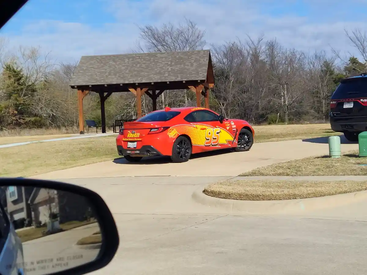 A red Toyota sports car, modified with Lightning McQueen's iconic #95 racing livery from the movie Cars, is parked in a…