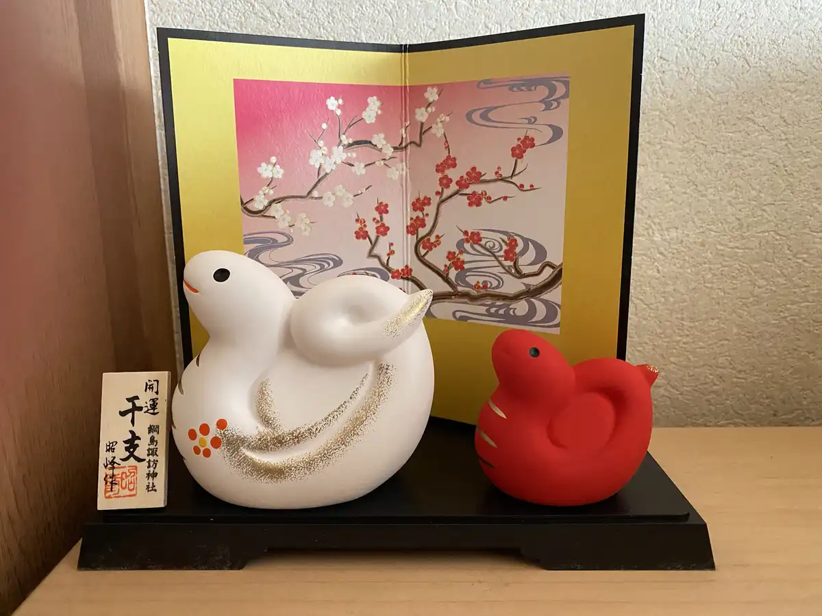 Two stylized ceramic duck figurines, one white with gold accents and one solid red, sit on a black stand in front of a…