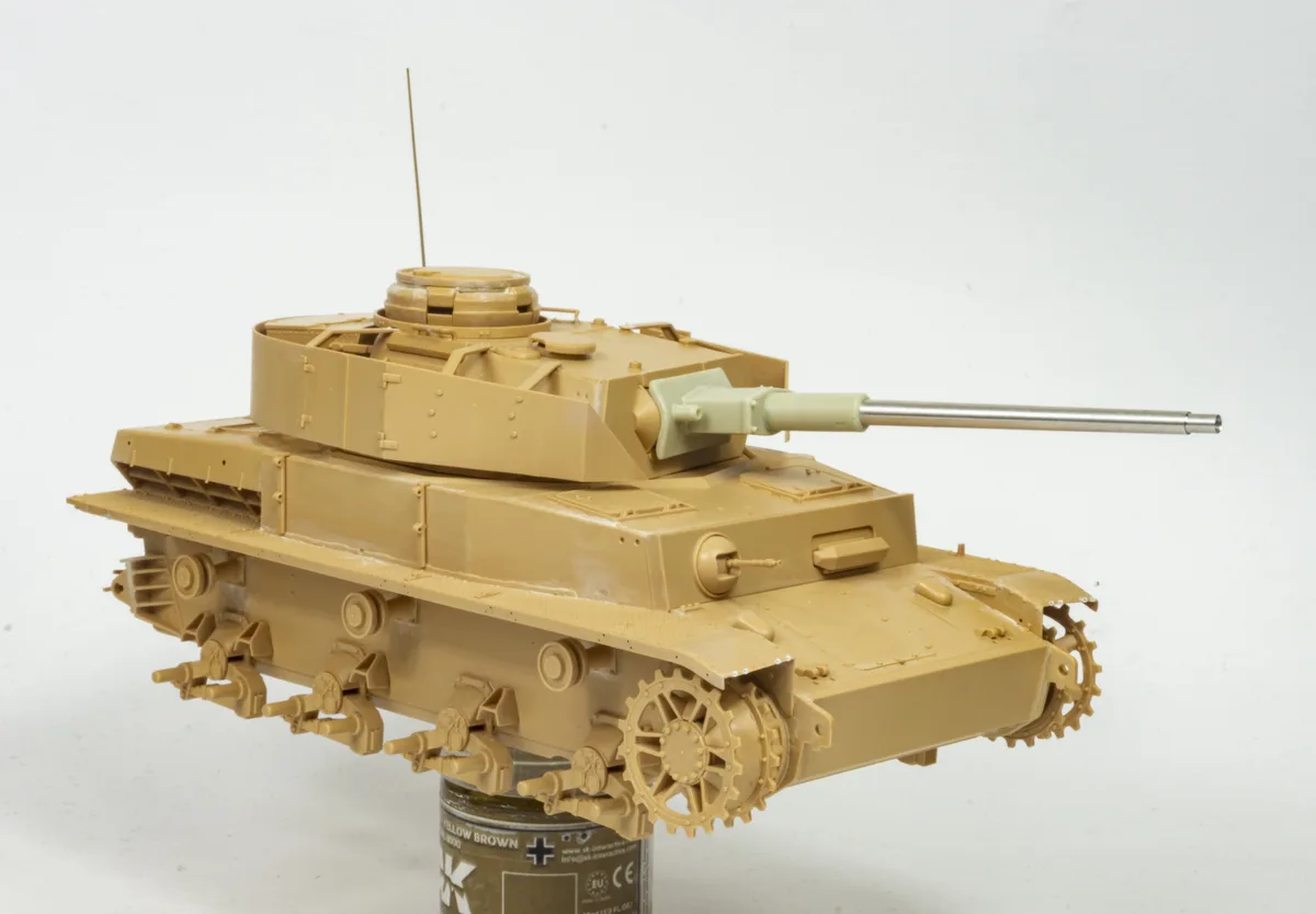 A detailed scale model of a tan-colored tank is mounted on top of a paint can labeled 'YELLOW BROWN'. The tank is shown in…