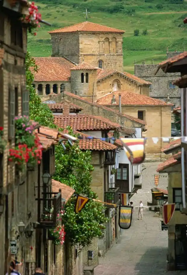 A picturesque view of a narrow cobblestone street in a historic European town, flanked by stone buildings with red-tiled…