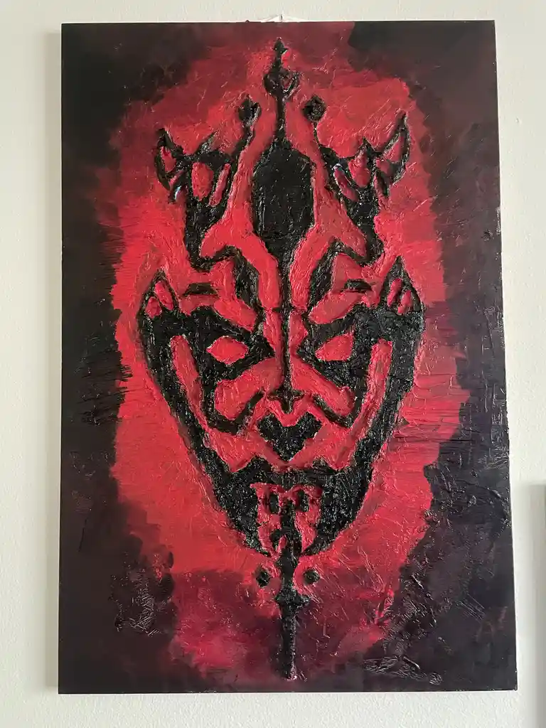 A textured painting on canvas depicts a stylized demonic face with horns, sharp features, and a crown-like top, rendered in…
