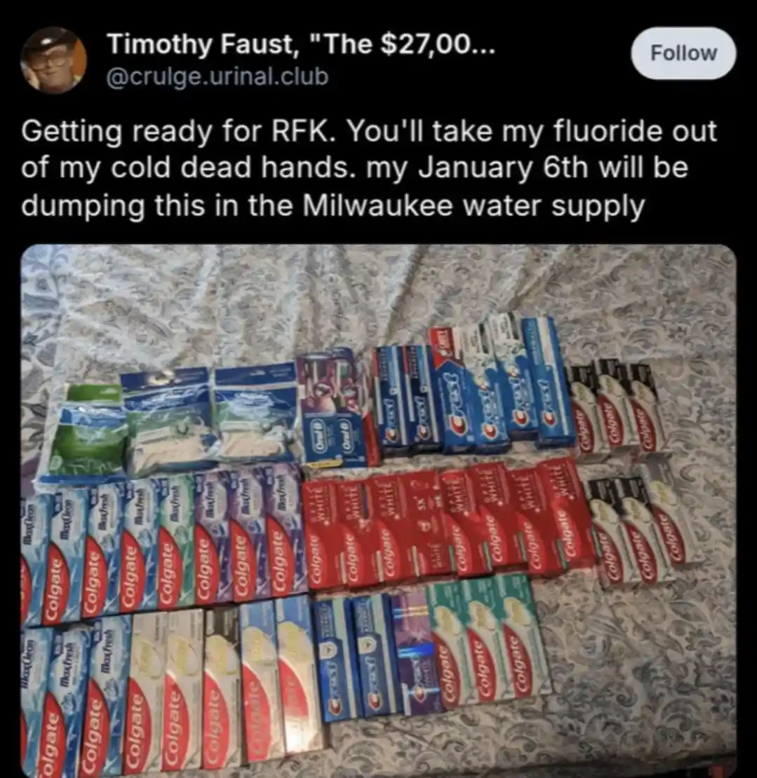 An overhead photo shows dozens of toothpaste tubes and toothbrushes arranged in rows on a patterned fabric surface. The…