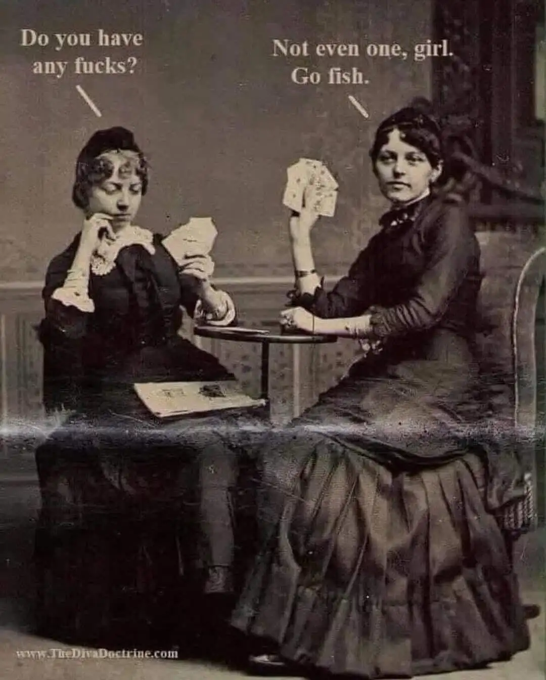 Two women in vintage 19th-century dresses sit at a small table playing cards. The woman on the left, looking down at her…
