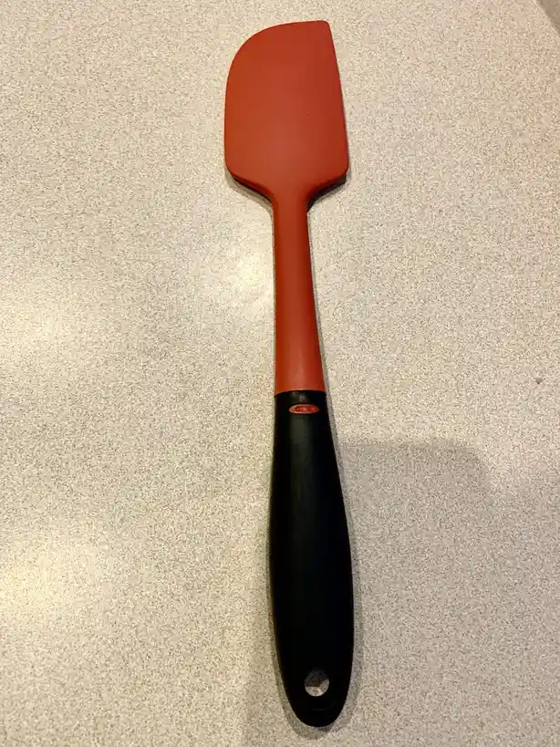 A red silicone spatula with a black handle rests on a speckled gray countertop. The overlaid text reads 'i'm not a fan of…