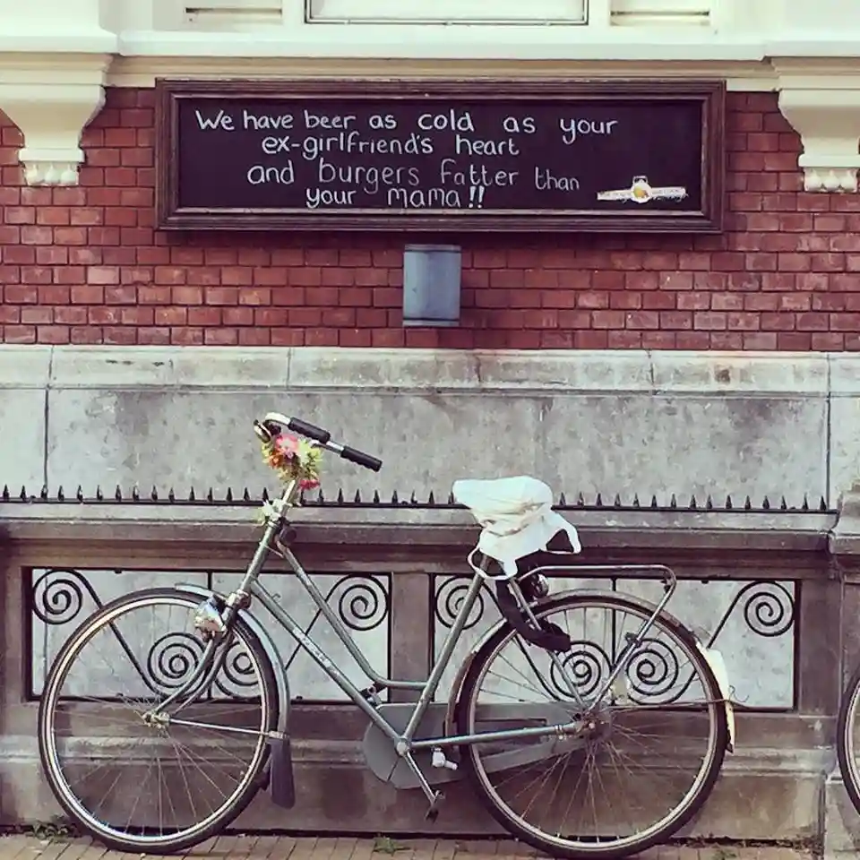 A vintage-style bicycle with a floral arrangement on the handlebars and a white cloth draped over the seat leans against a…