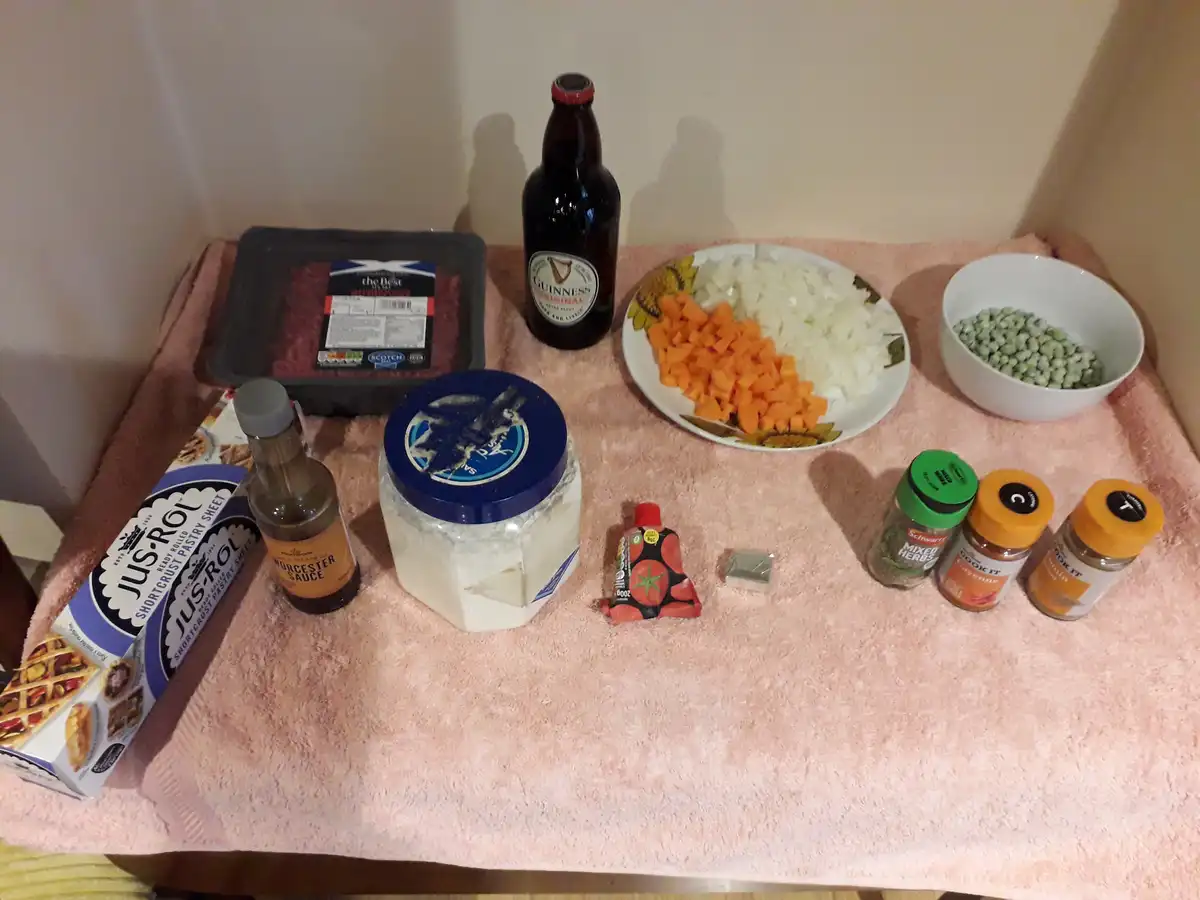 A collection of cooking ingredients including a bottle of Guinness beer, a package of ground beef, a plate with chopped…