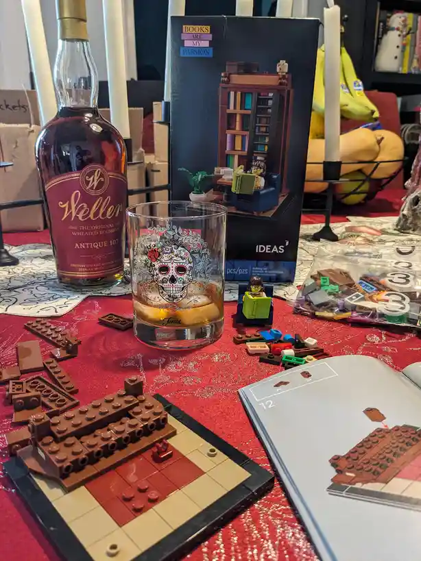A table scene features a bottle of Weller Antique 107 bourbon next to a glass with a sugar skull design, surrounded by…