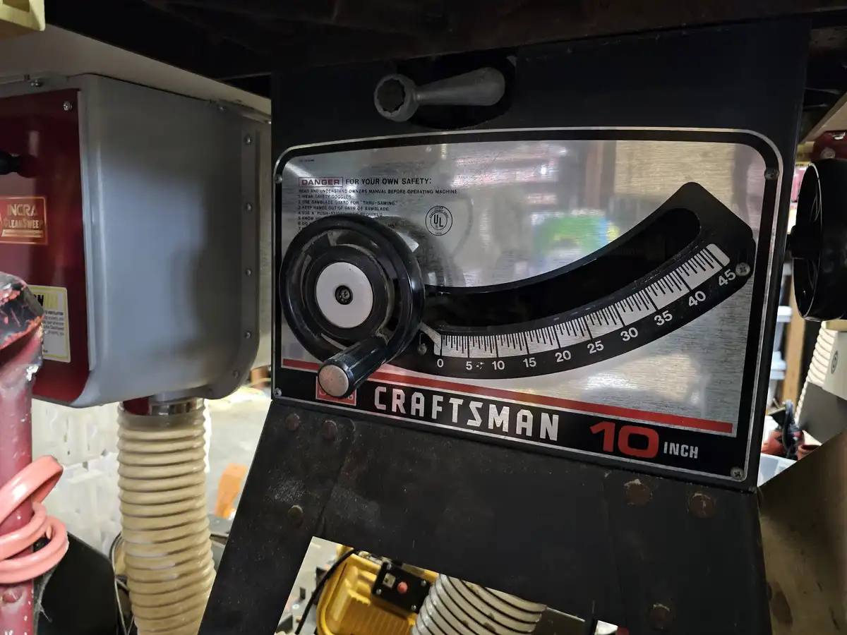 A close-up of a Craftsman 10-inch table saw's bevel adjustment scale, showing a black curved ruler marked from 0 to 45…