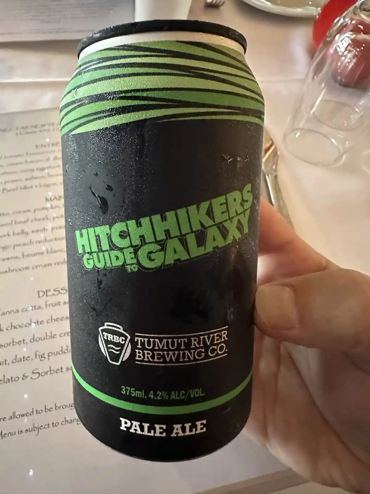 A hand holds a chilled, condensation-covered beer can labeled 'Hitchhikers Guide to the Galaxy' by Tumut River Brewing Co…