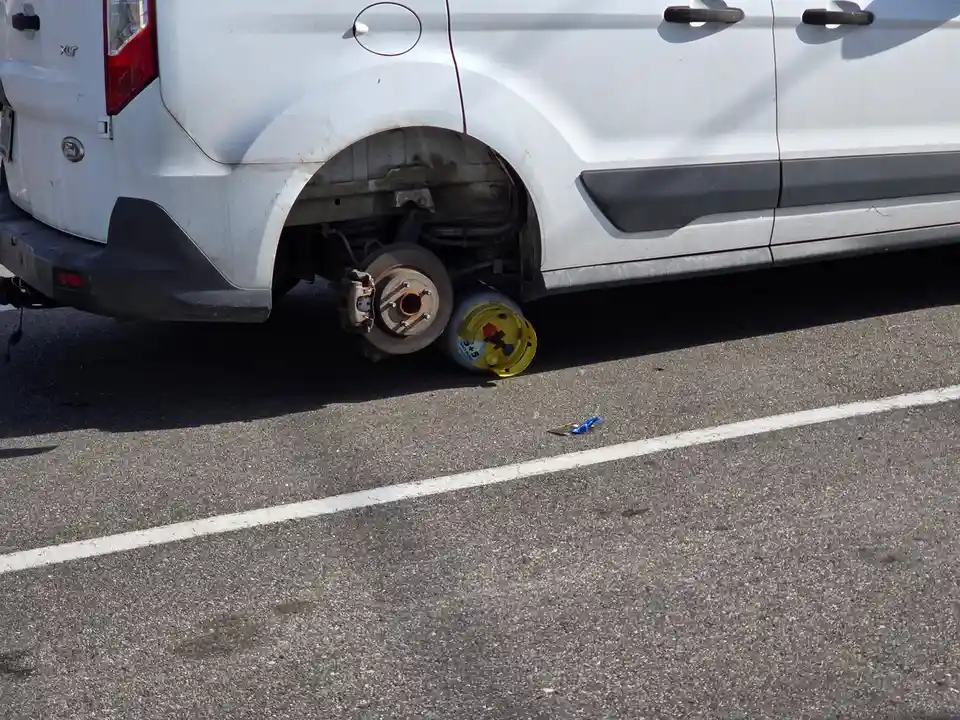 A white Ford van has its rear wheel removed, exposing the brake rotor and suspension. A yellow and white compressed gas…