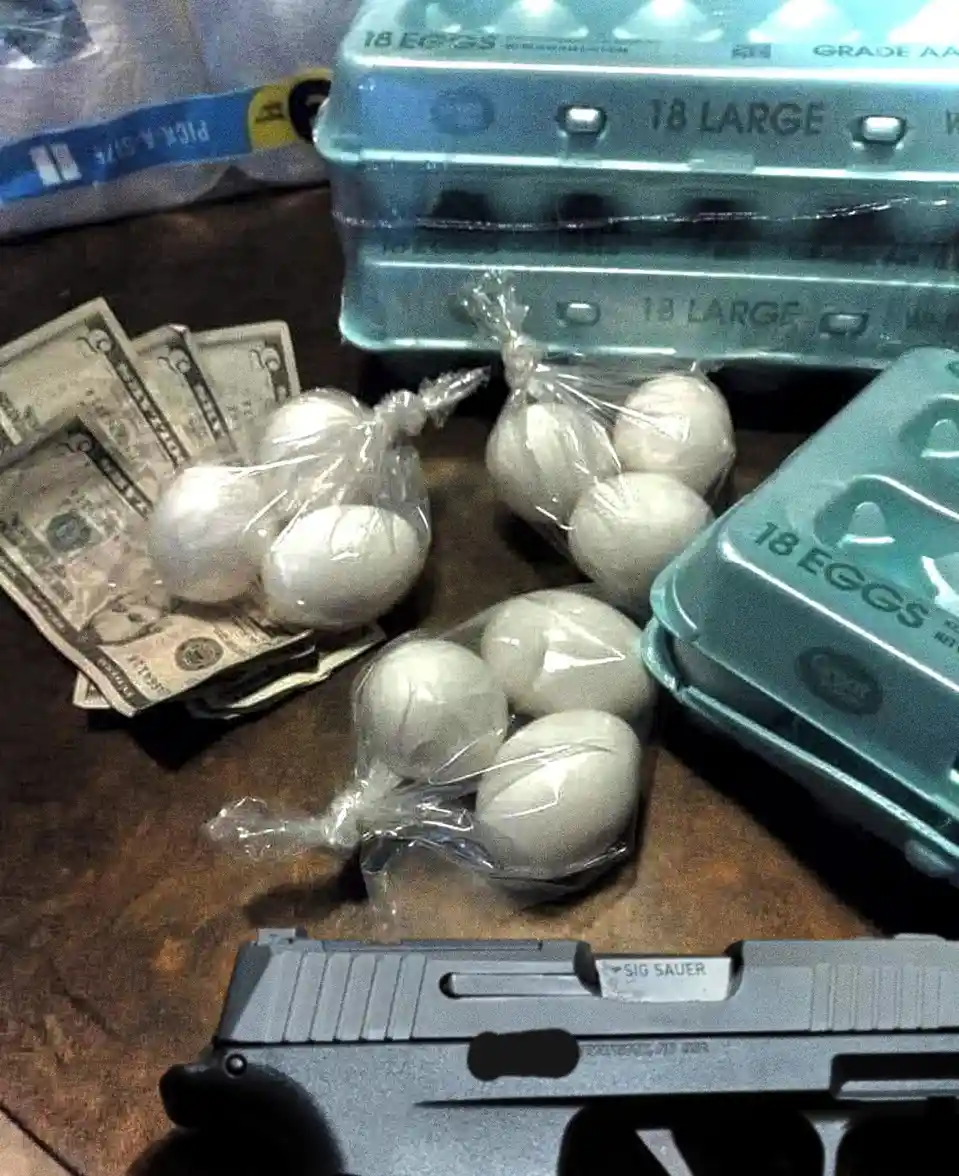 A close-up photo shows a pile of US dollar bills next to several clear plastic bags filled with white eggs, with multiple…