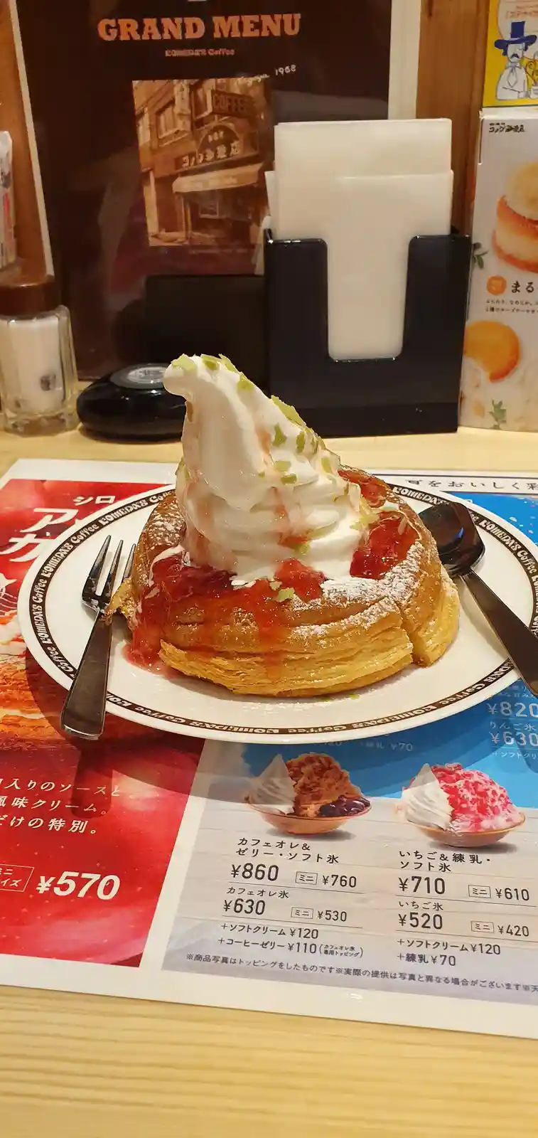 A close-up photo of a Comedia's Coffee strawberry cream puff dessert, topped with whipped cream and green sprinkles, served…