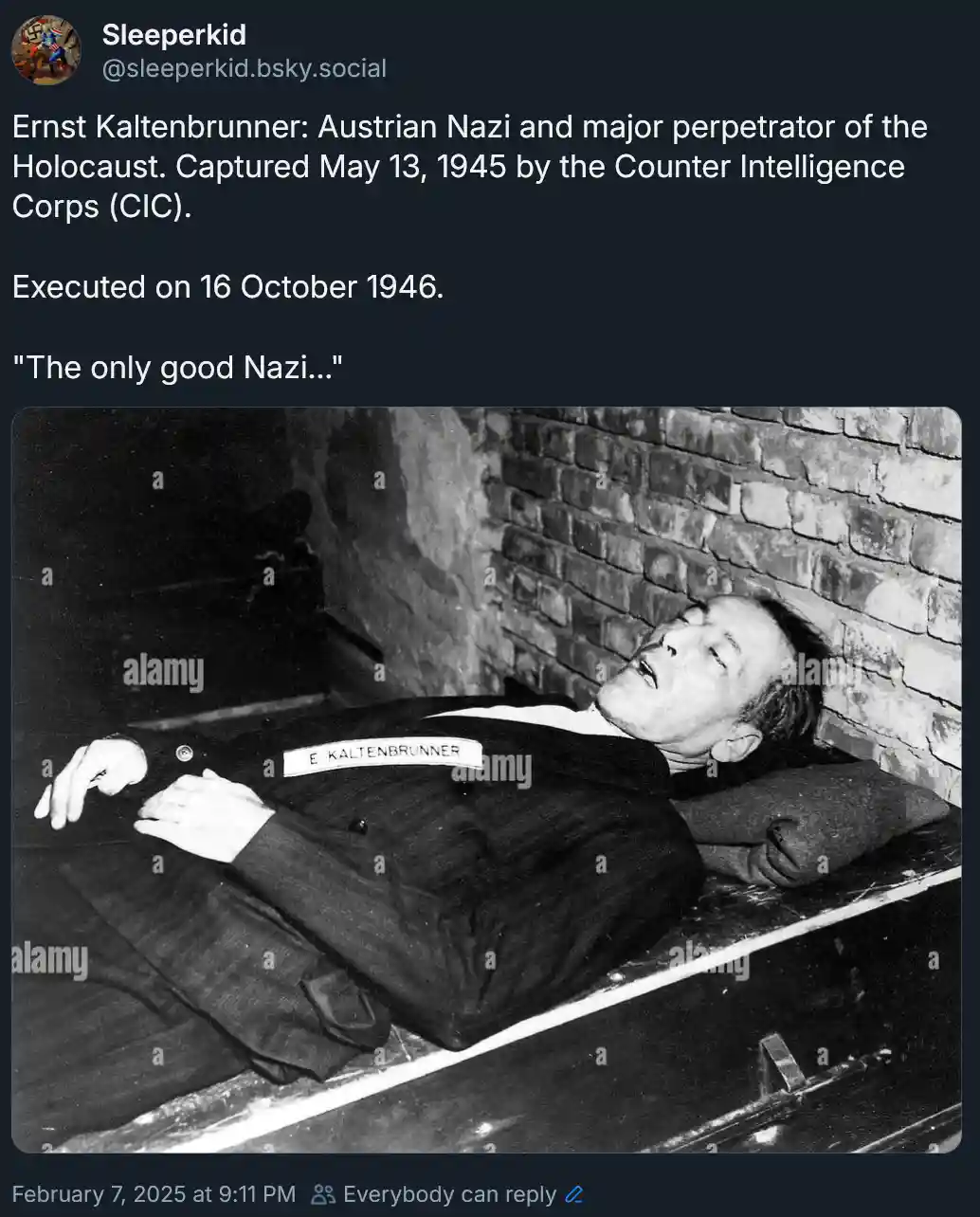 A black-and-white historical photo shows a man in a suit lying on his back on a wooden surface, head resting against a brick…